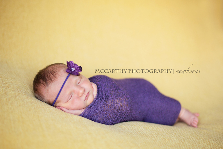 newborn baby posed with hands to her face and wrapped in purple
